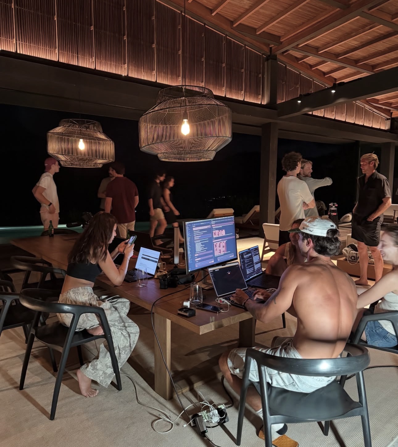 People working on laptops and talking around a table in an open villa at night